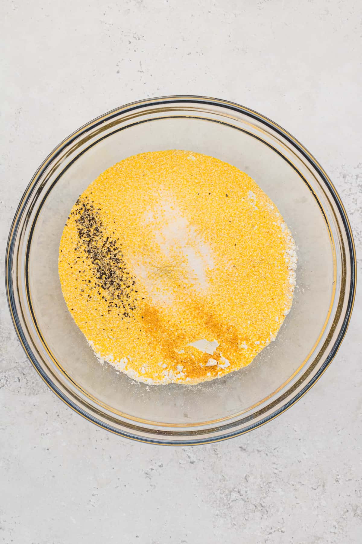 Dry ingredients - cornmeal, Bisquick, salt, pepper, garlic powder - measured into a mixing bowl for Savory Breakfast Muffins.