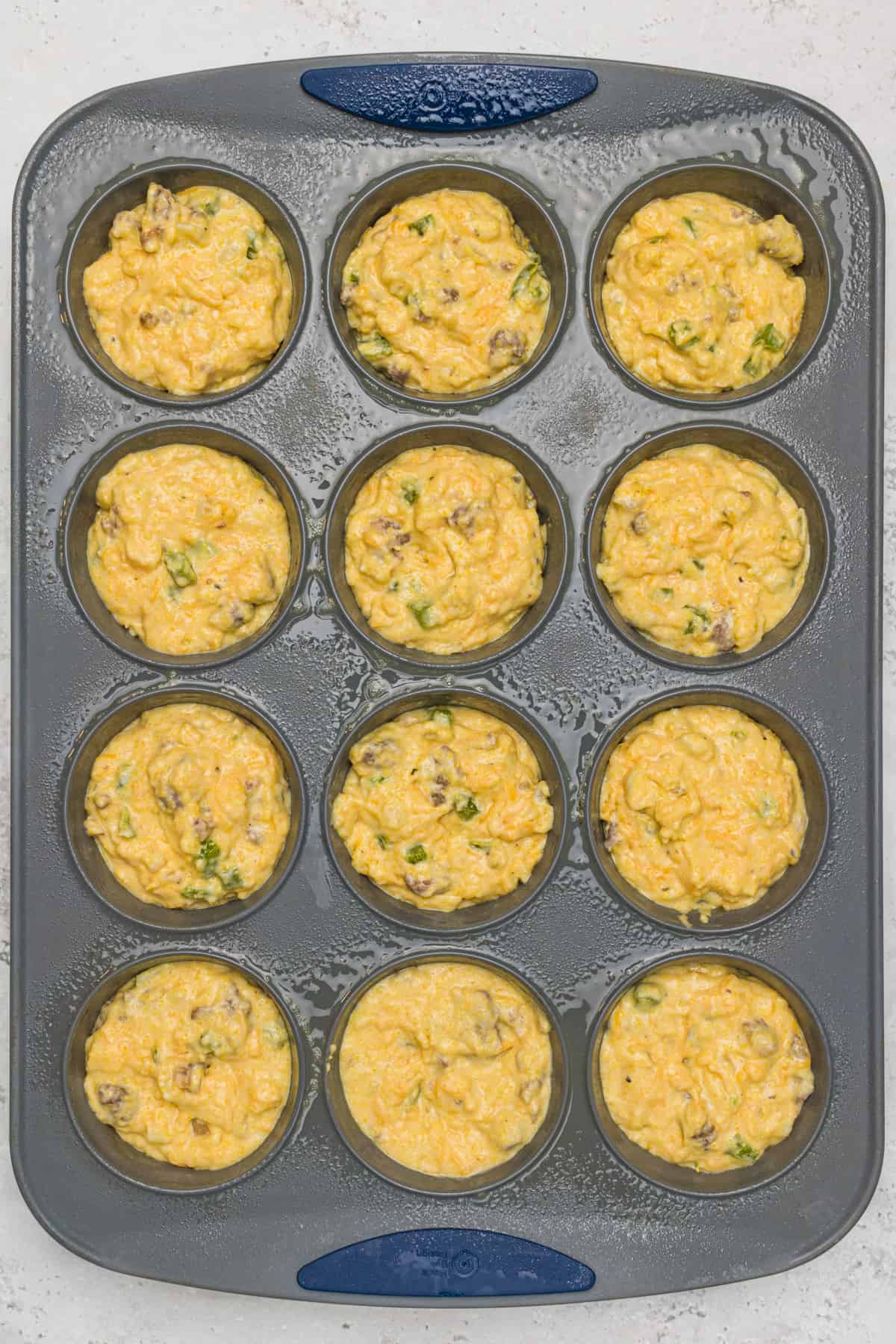 Muffin tin sprayed with cooking spray and holding uncooked Savory Breakfast Muffin mix in each cup ready to be baked.
