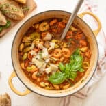 Italian sausage and tortellini soup fully cooked in a dutch oven with Parmesan cheese shavings and fresh basil on top.