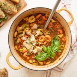 Italian sausage and tortellini soup fully cooked in a dutch oven with Parmesan cheese shavings and fresh basil on top.