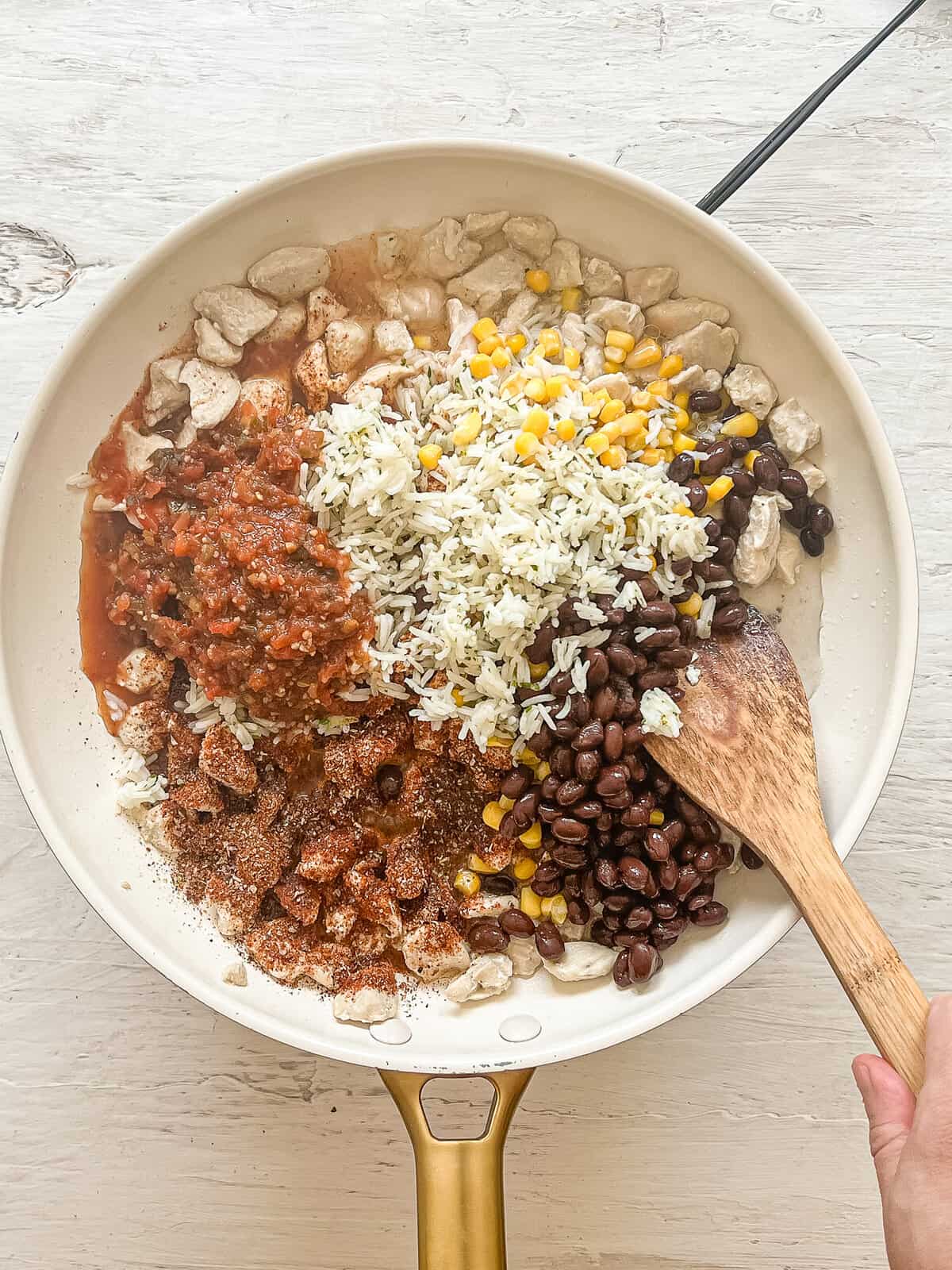 Rice, beans, corn, seasonings, and salsa on top of cooked chicken in a ceramic skillet ready to be mixed for Chicken Burritos.