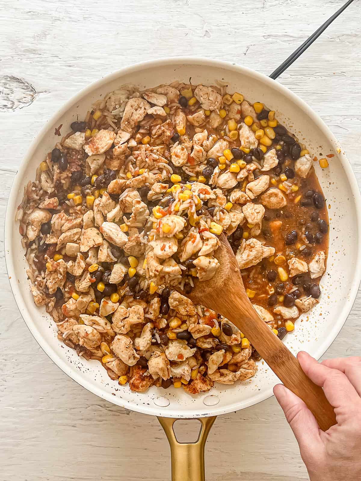 Ingredients (rice, corn, cooked chicken, salsa, black beans and seasonings) being mixed together in a ceramic skillet for Chicken Burritos