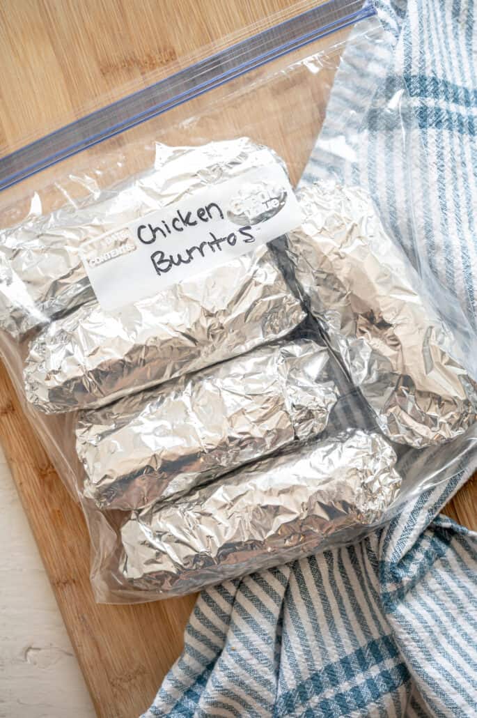 Chicken Burritos wrapped in foil and inside a freezer bag laying on a cutting board.