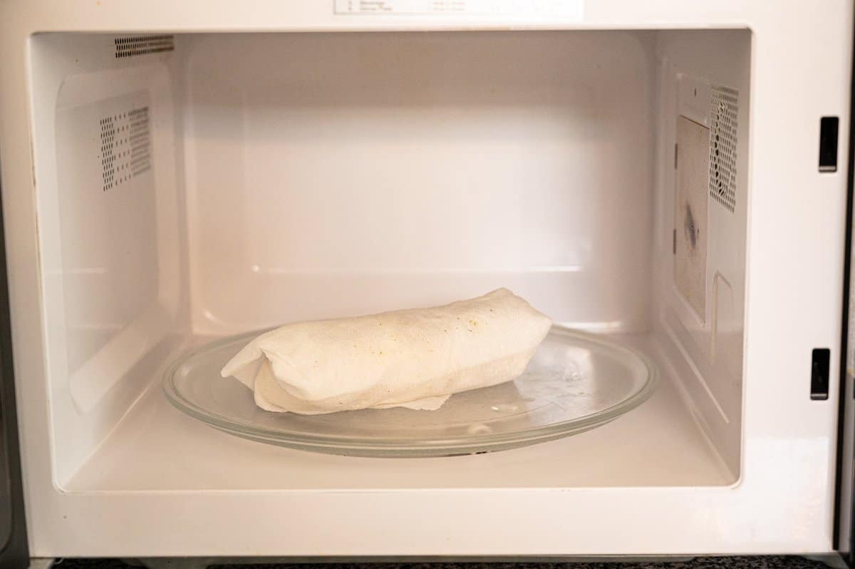 Chicken Burrito wrapped in a damp paper towel inside a microwave.