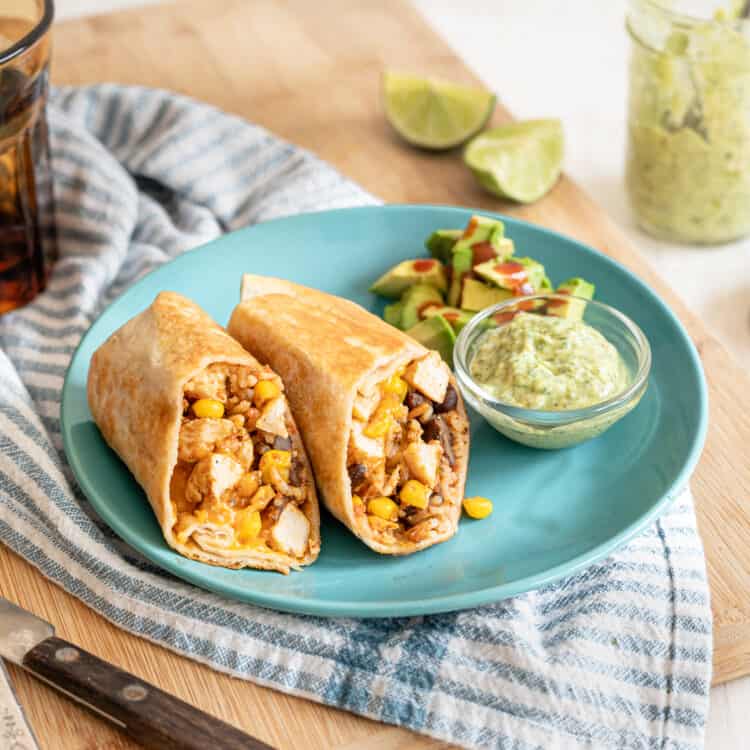 Chicken Burrito sliced in half on an aqua plate that is sitting on a wooden cutting board.