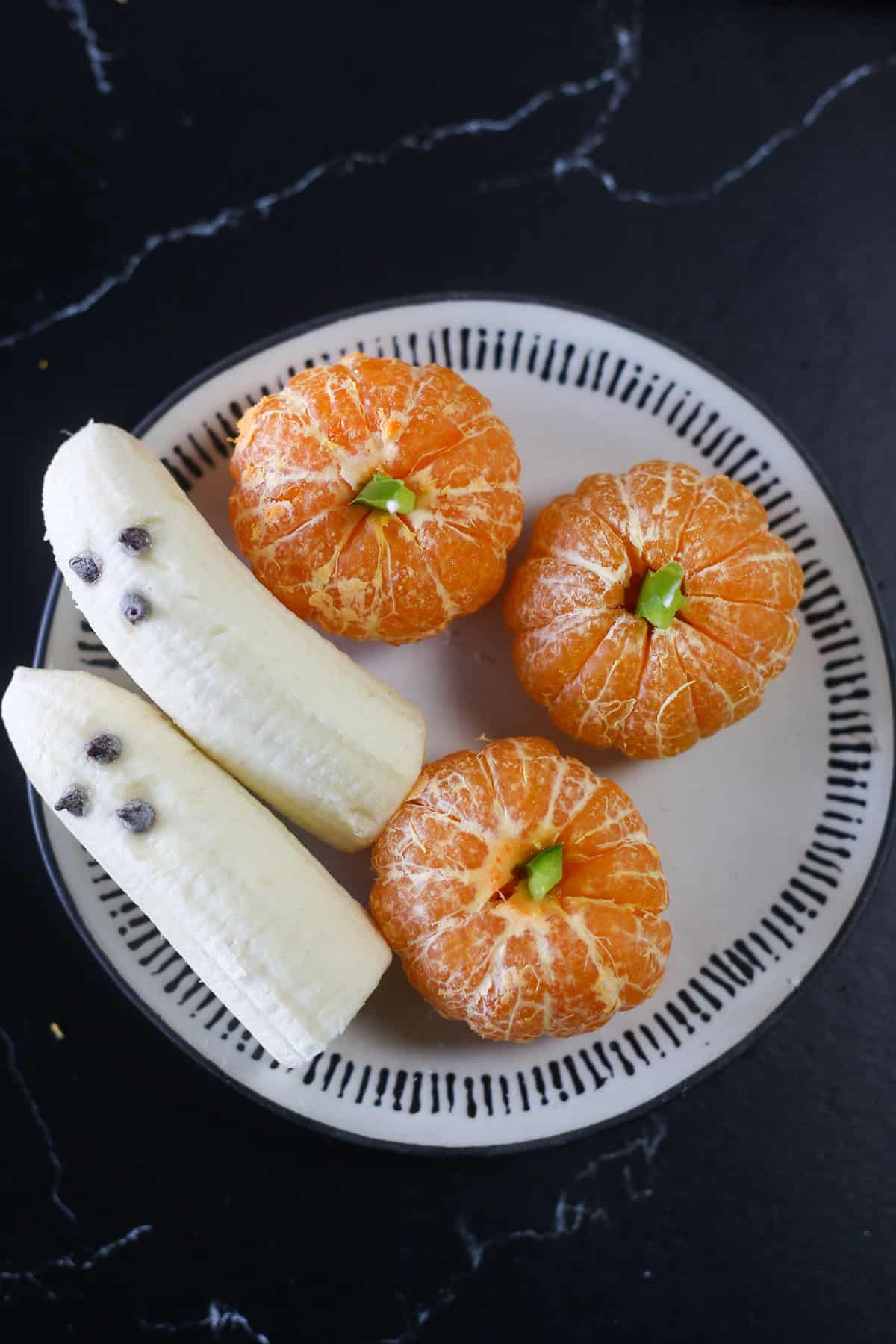 Three clementine pumpkins on a plate with ghost bananas.