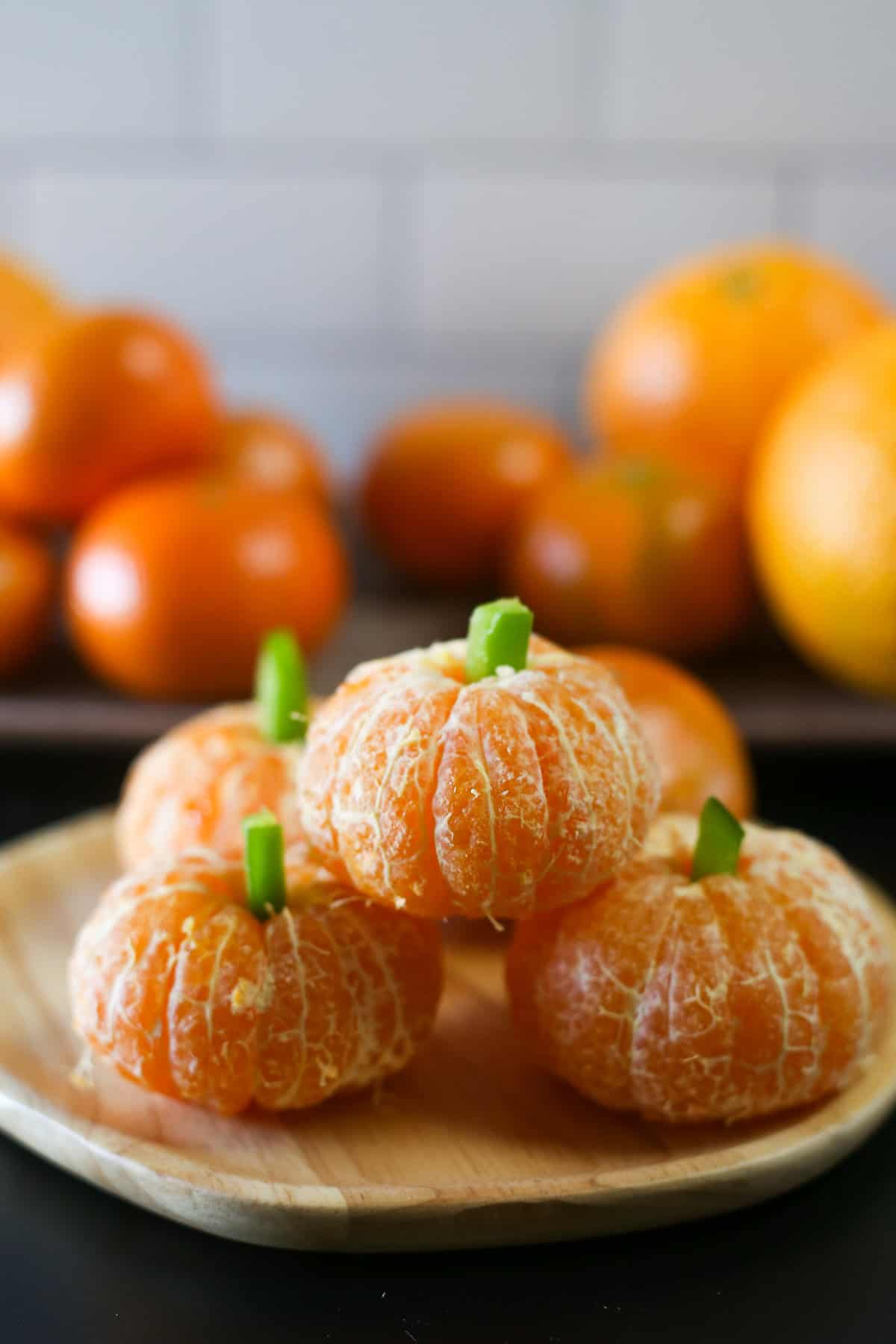 Clementine pumpkins stacked up with oranges in the background.