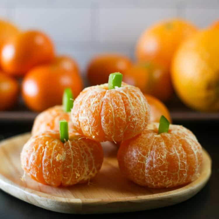 Clementine pumpkins stacked up with oranges in the background.