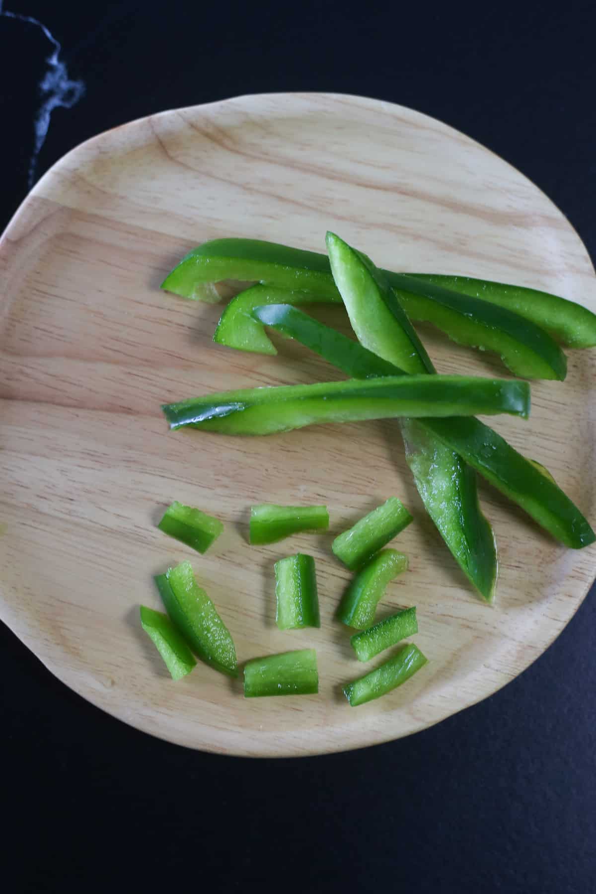 Green peppers sliced up on a wooden plate.