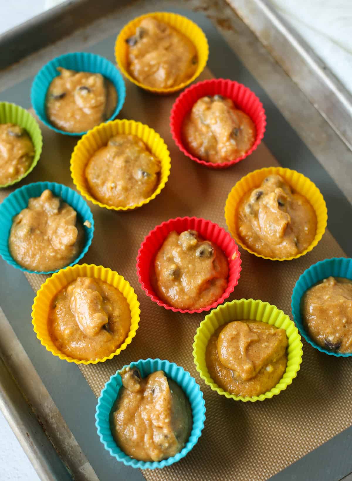 Gluten-free pumpkin muffin batter in silicone muffin liners on a baking sheet. 