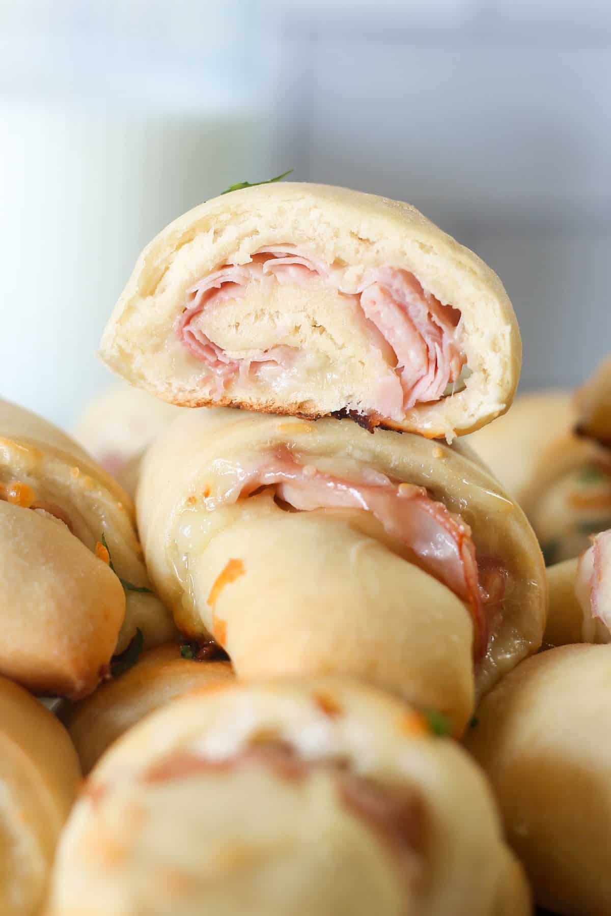 A ham and cheese crescent roll sliced in half on top of a stack of others.