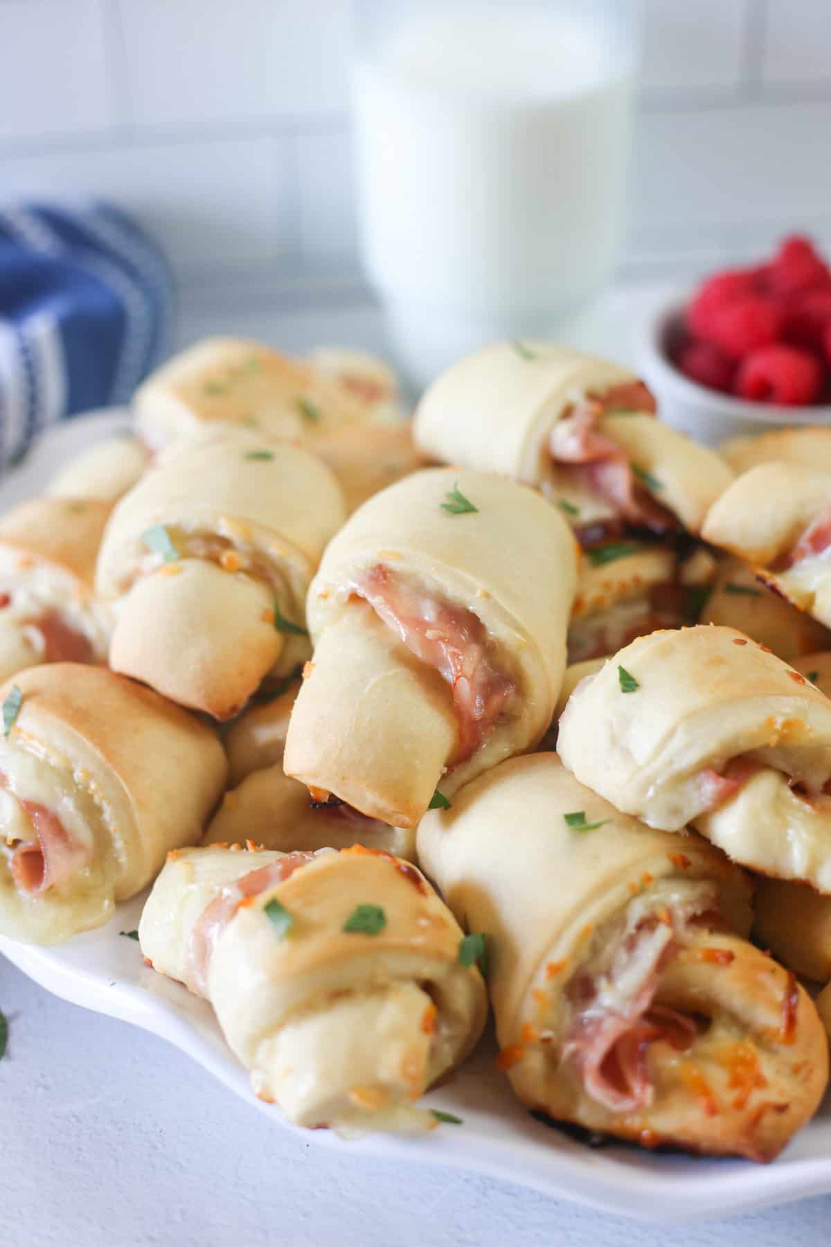Ham and cheese crescent rolls piled up on a plate with raspberries in the background.