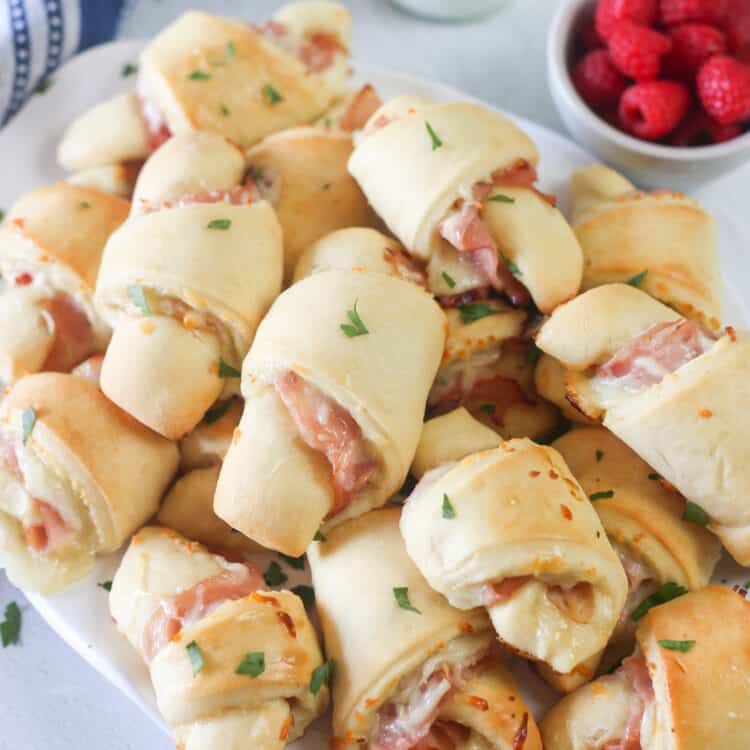 A large pile of ham and cheese croissants on a white platter.