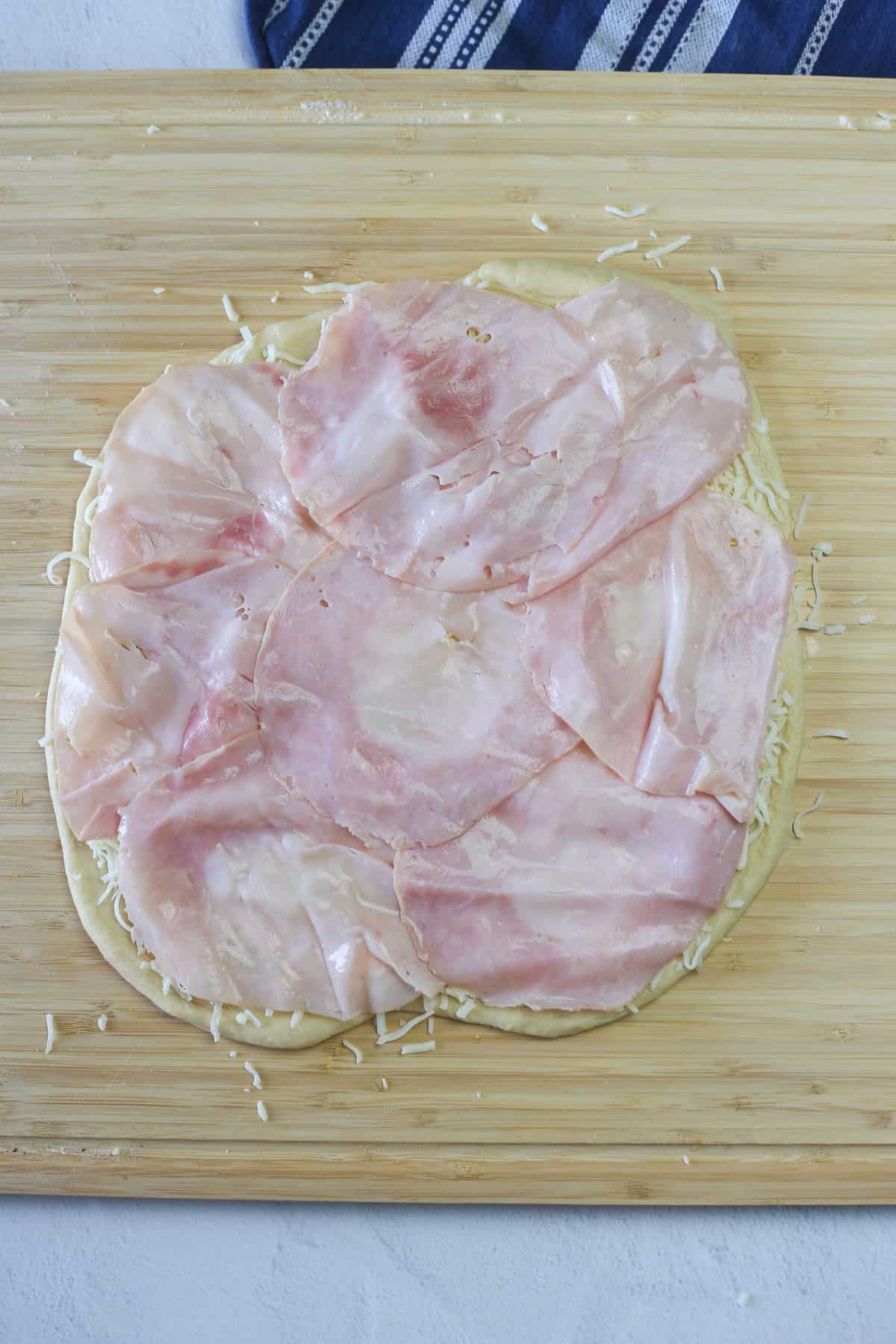 A layer of ham on top of shredded cheese and dough.