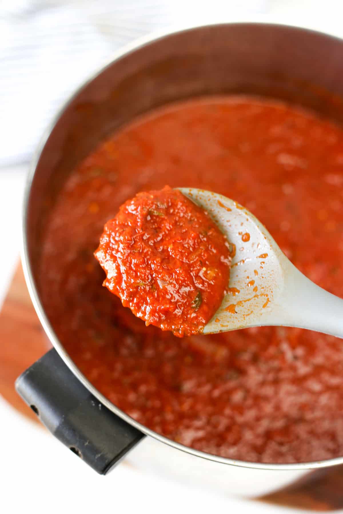 A spoon scooping out marinara sauce from a pot.