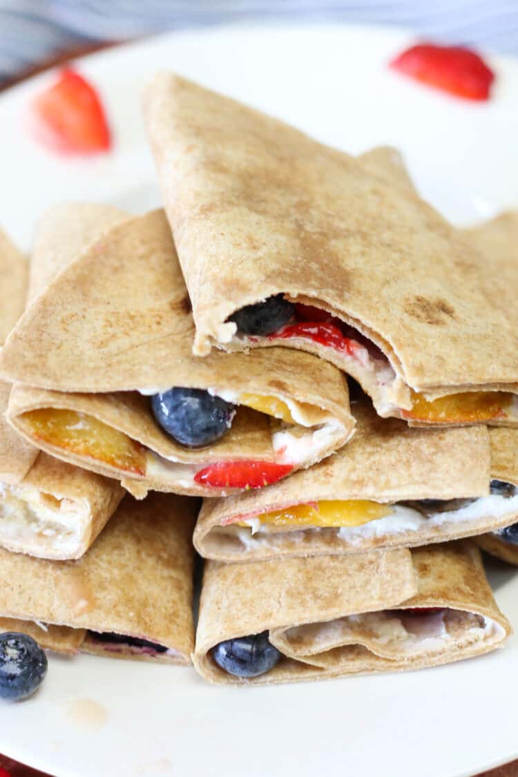 Fruit pizza roll ups stacked with one having a bite taken out of it.