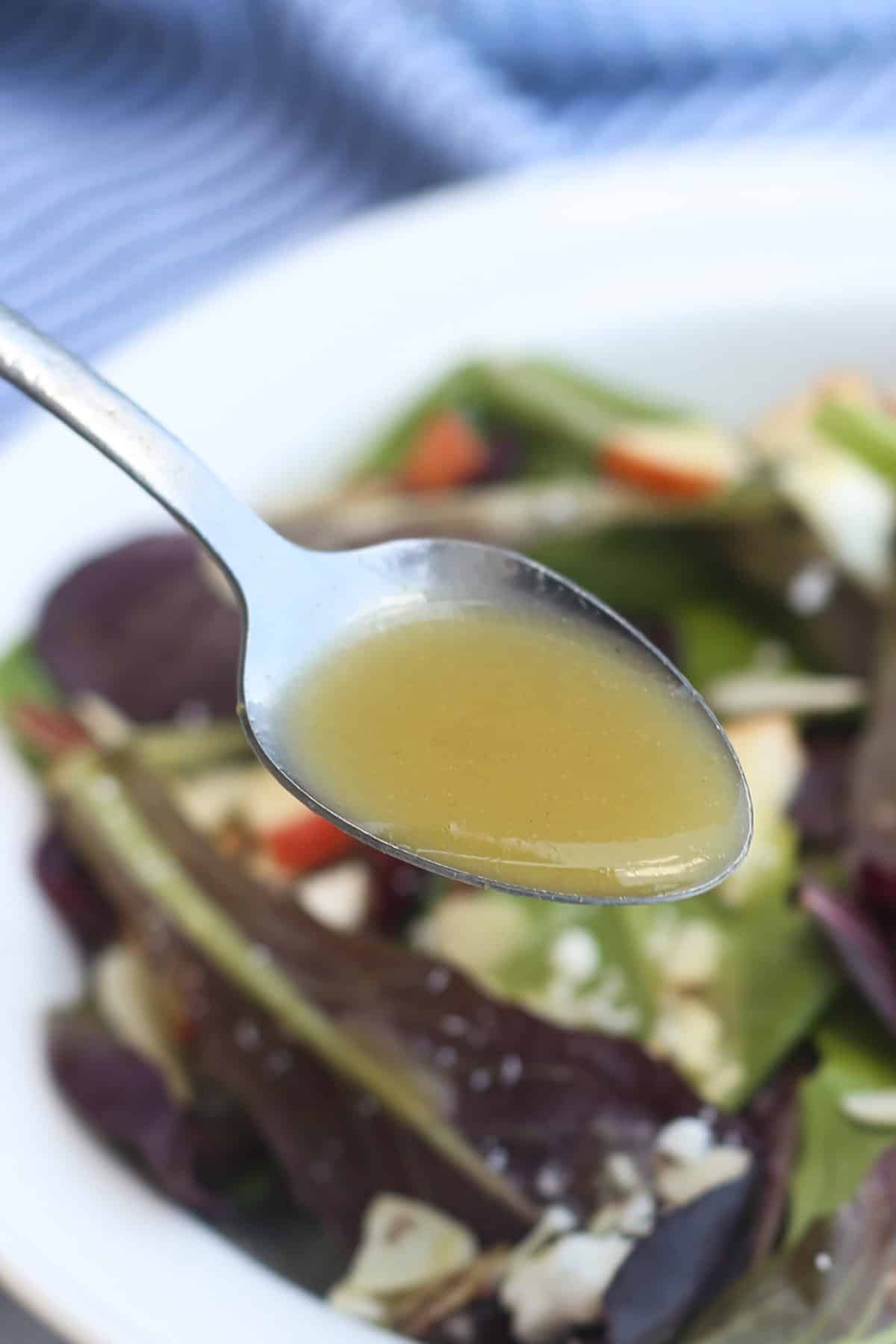 Spoon drizzling honey dijon dressing on top of a red and green leaf salad.