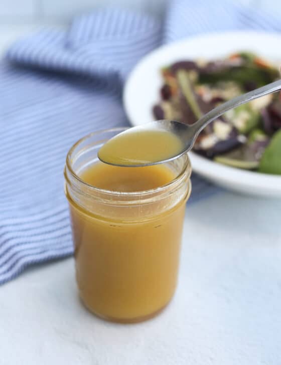 Honey Dijon salad dressing in a mason jar with a spoon scooping some out.