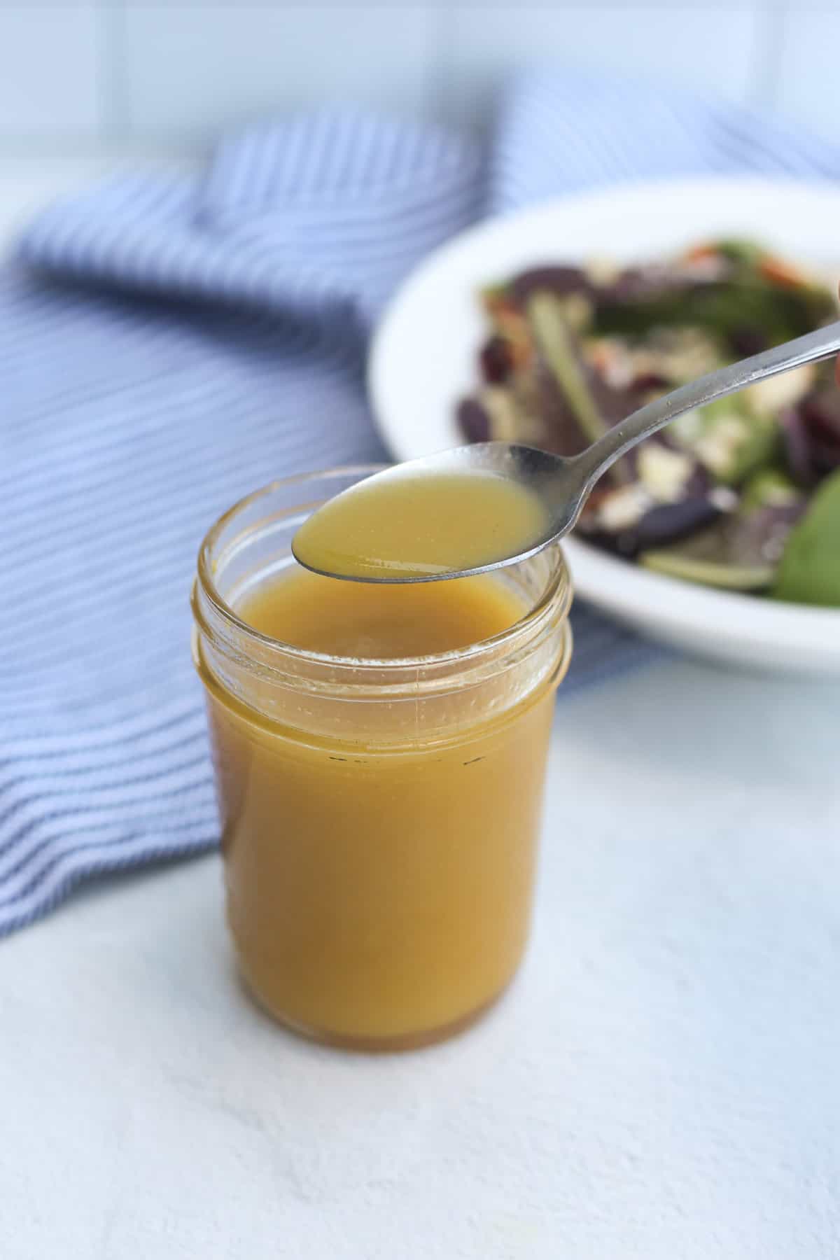 Honey Dijon salad dressing in a mason jar with a spoon scooping some out. 