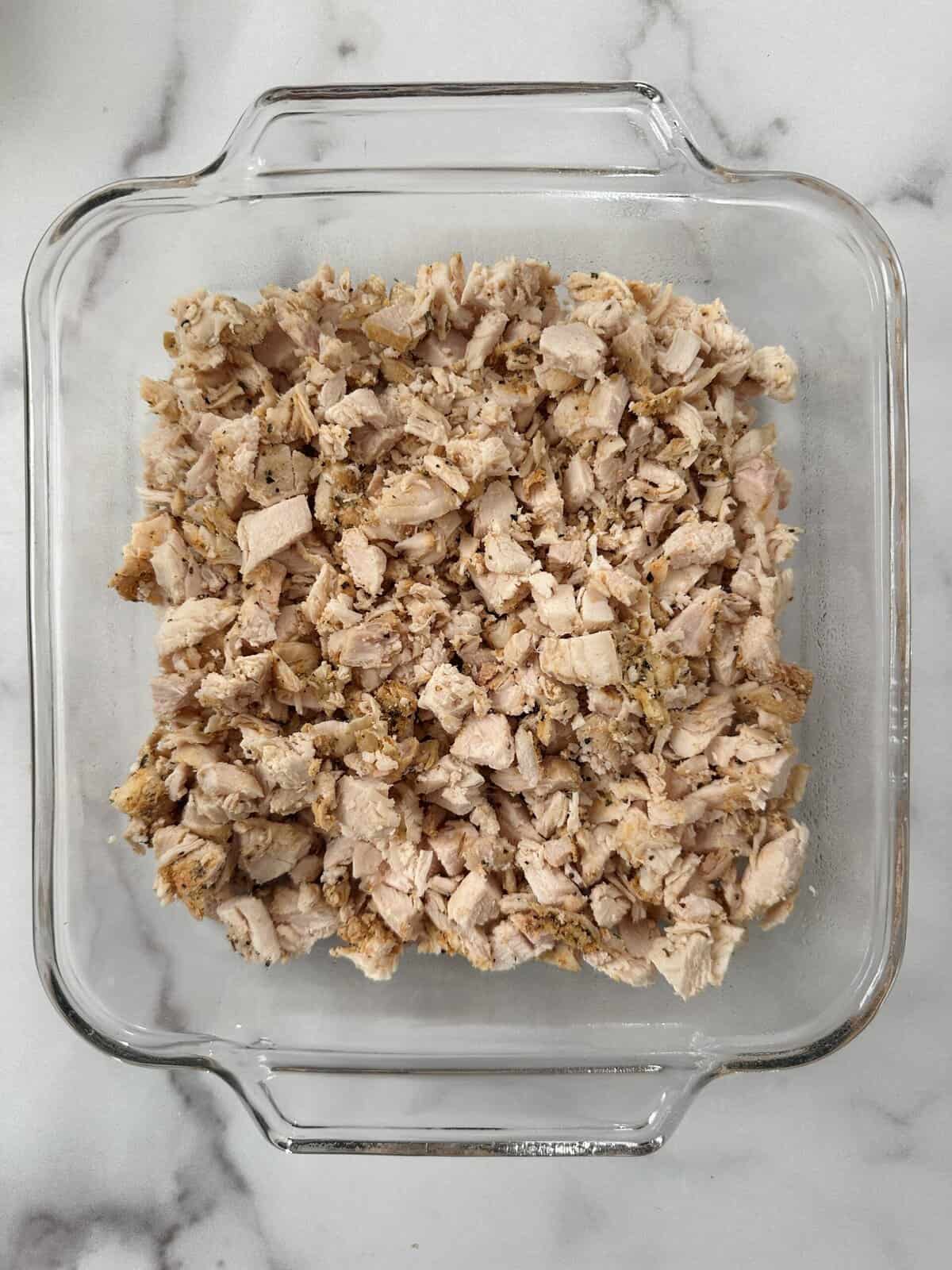 Chopped, cooked chicken in the bottom of a square casserole dish.