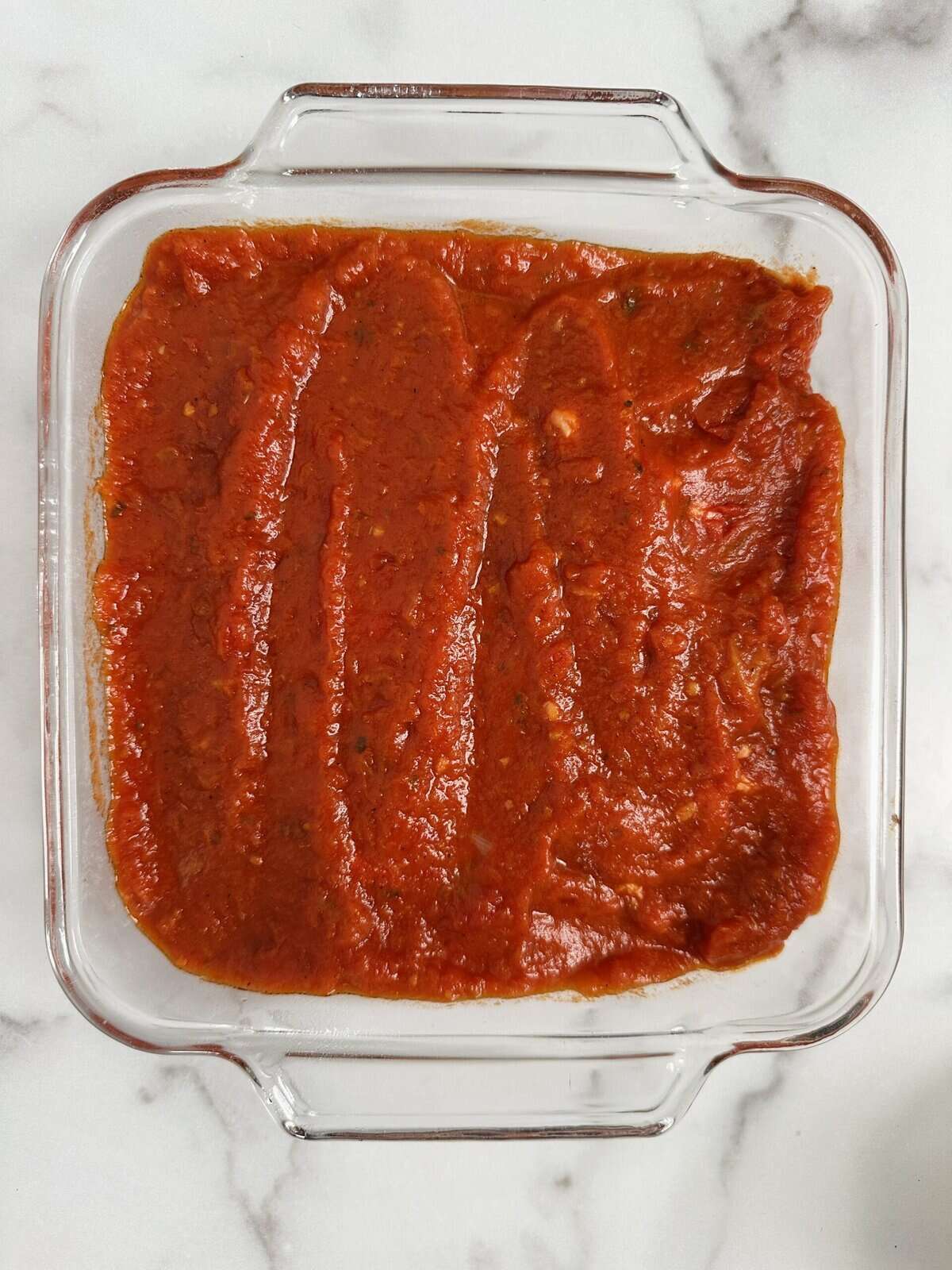 Marinara sauce spread over the top of the chopped chicken in casserole dish.