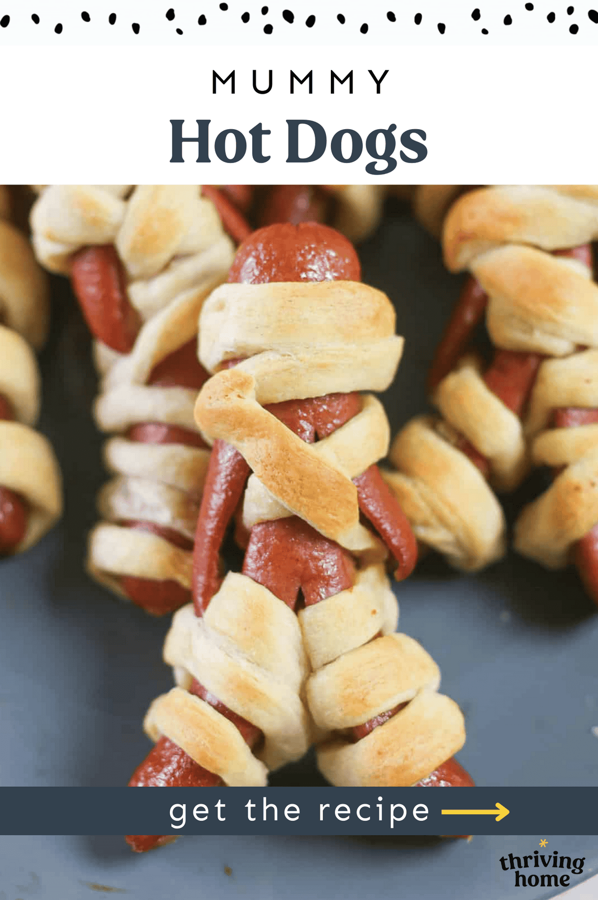 A mummy hotdog set in front of more mummy hotdogs on a platter.
