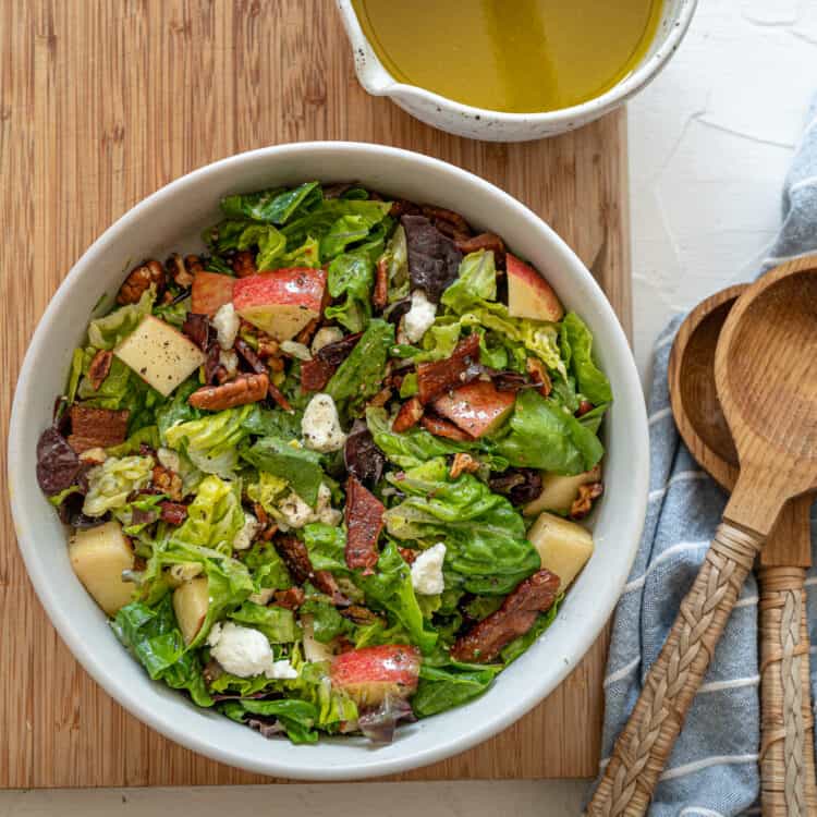 Autumn Salad tossed with apple cider vinaigrette in a white bowl on a wooden cutting board.