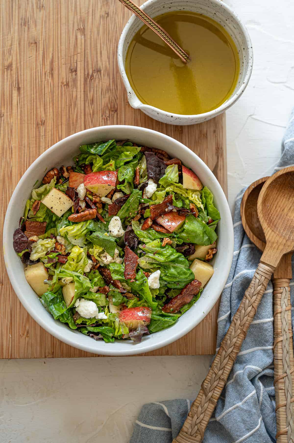 Autumn Salad tossed with apple cider vinaigrette in a white bowl on a wooden cutting board.