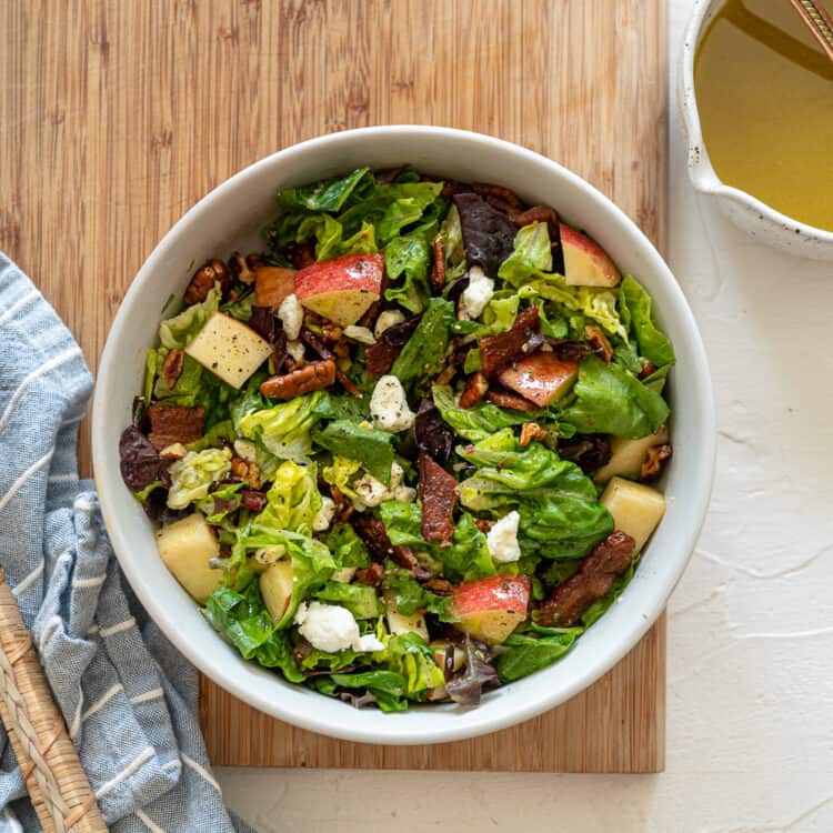 Autumn Salad tossed with apple cider vinaigrette in a white bowl sitting on a wooden cutting board.