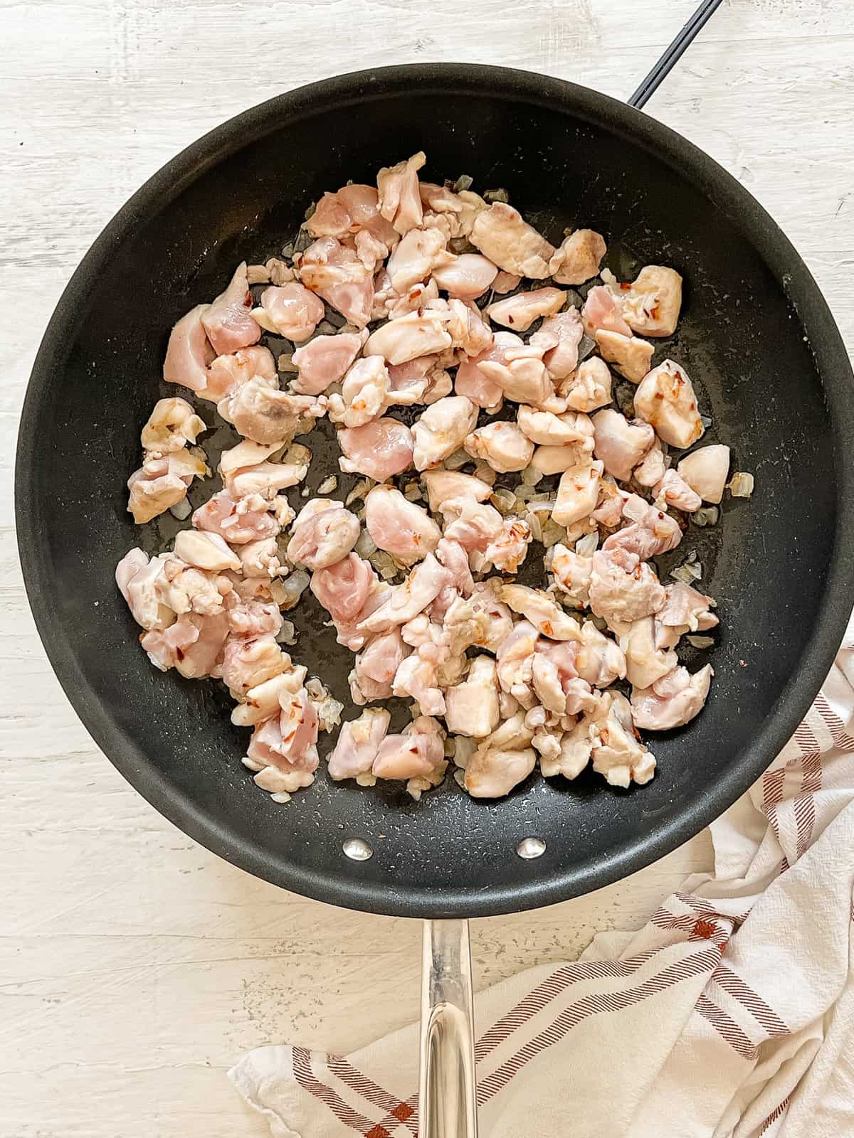 Cut up chicken sauteing with diced onion in a skillet.