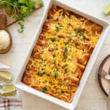 Cheesy Chicken Enchiladas baked in a white casserole dish on a wooden table.