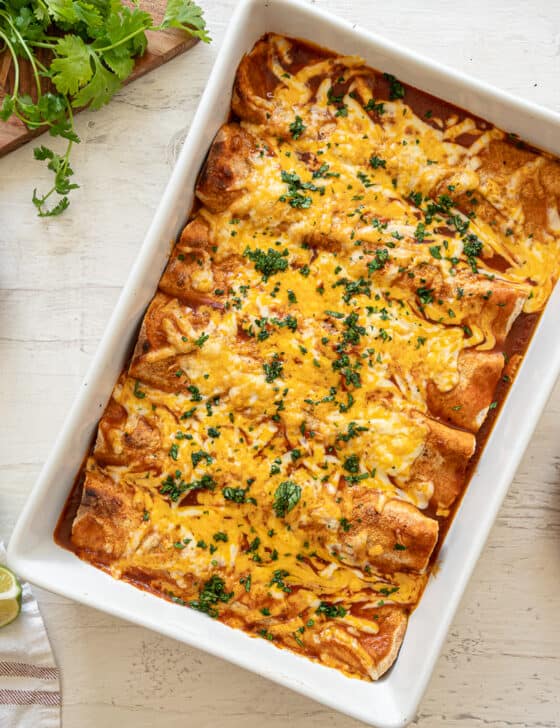 Cheesy Chicken Enchiladas baked in a white casserole dish on a wooden table.