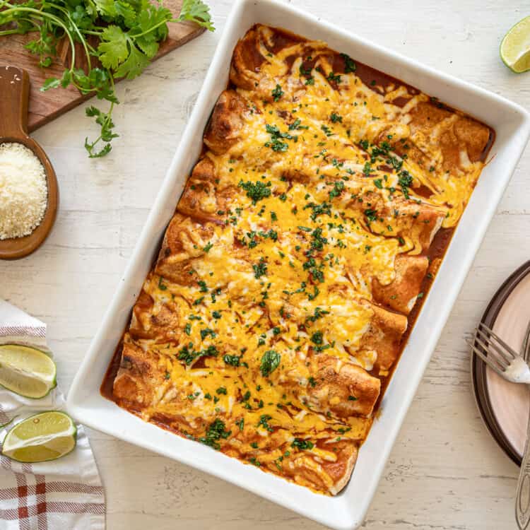 Cheesy Chicken Enchiladas baked in a white casserole dish on a wooden table.