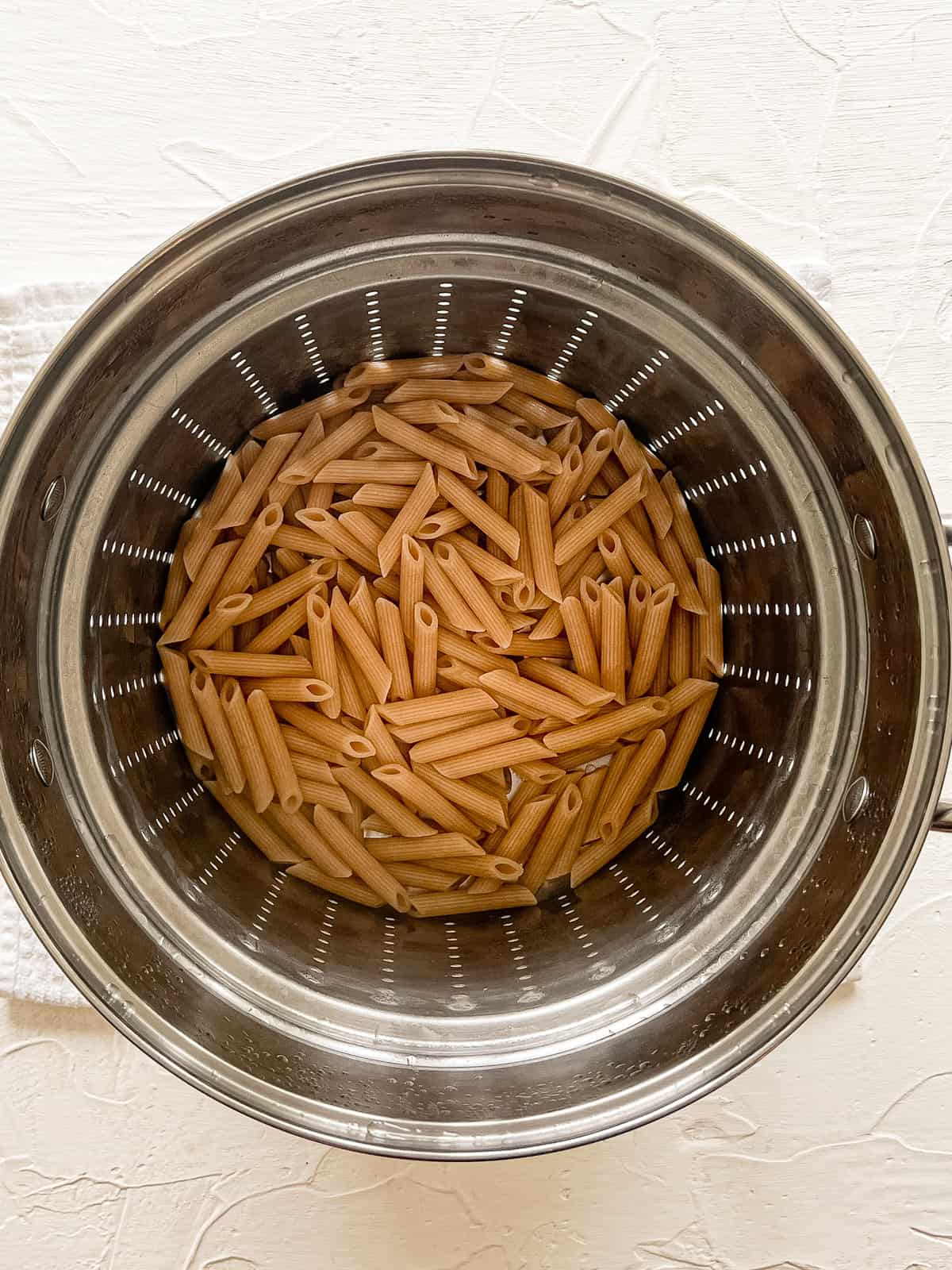 Cooked penne pasta in a stainless steel colander for Chicken Penne with Asparagus and Peppers.