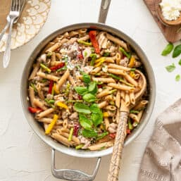 Chicken Penna Pasta with Asparagus and Peppers in a skillet with fresh basil and feta cheese on top ready to be served.