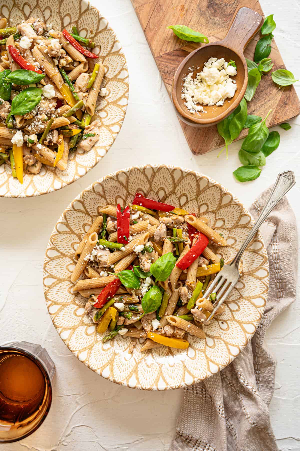 Chicken Penne with Asparagus and Peppers served on plates with fresh basil and feta cheese on top.