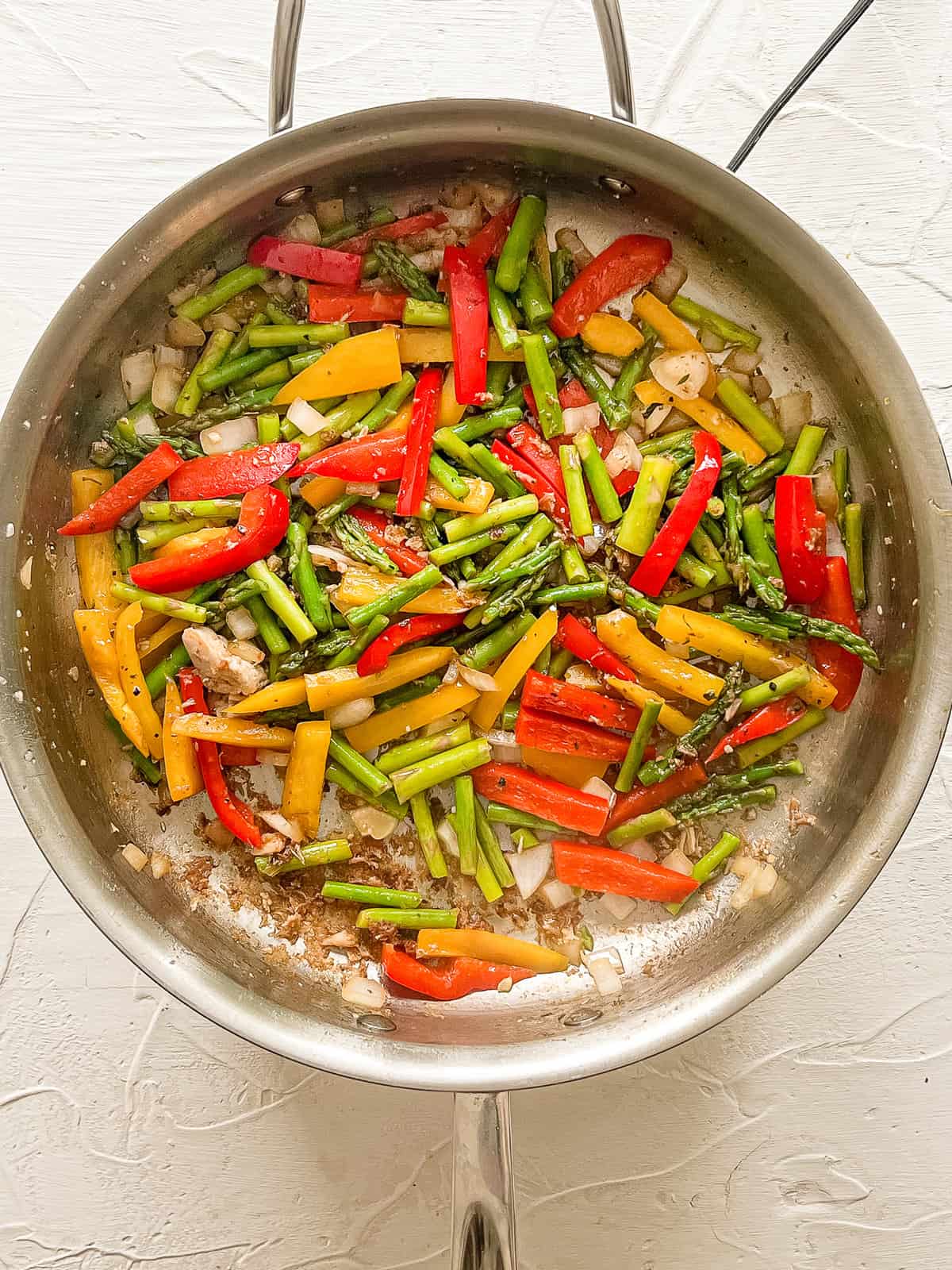 Onions, asparagus, red & yellow bell peppers sauteing in a stainless steel skillet.