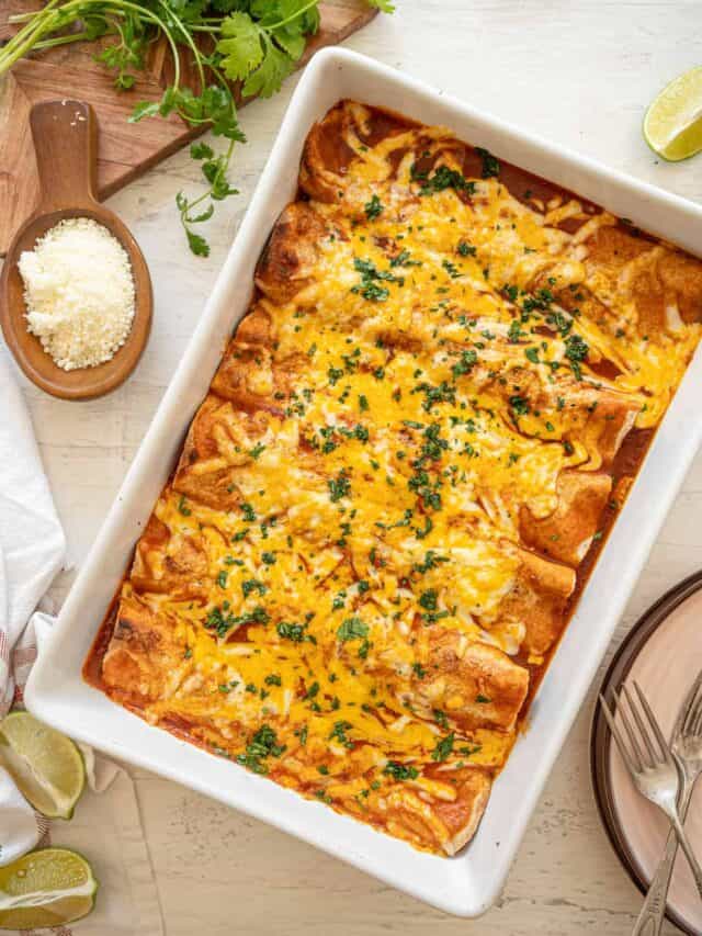 Cheesy Chicken Enchiladas baked in a white casserole dish with lime wedges and fresh cilantro on the table as well.