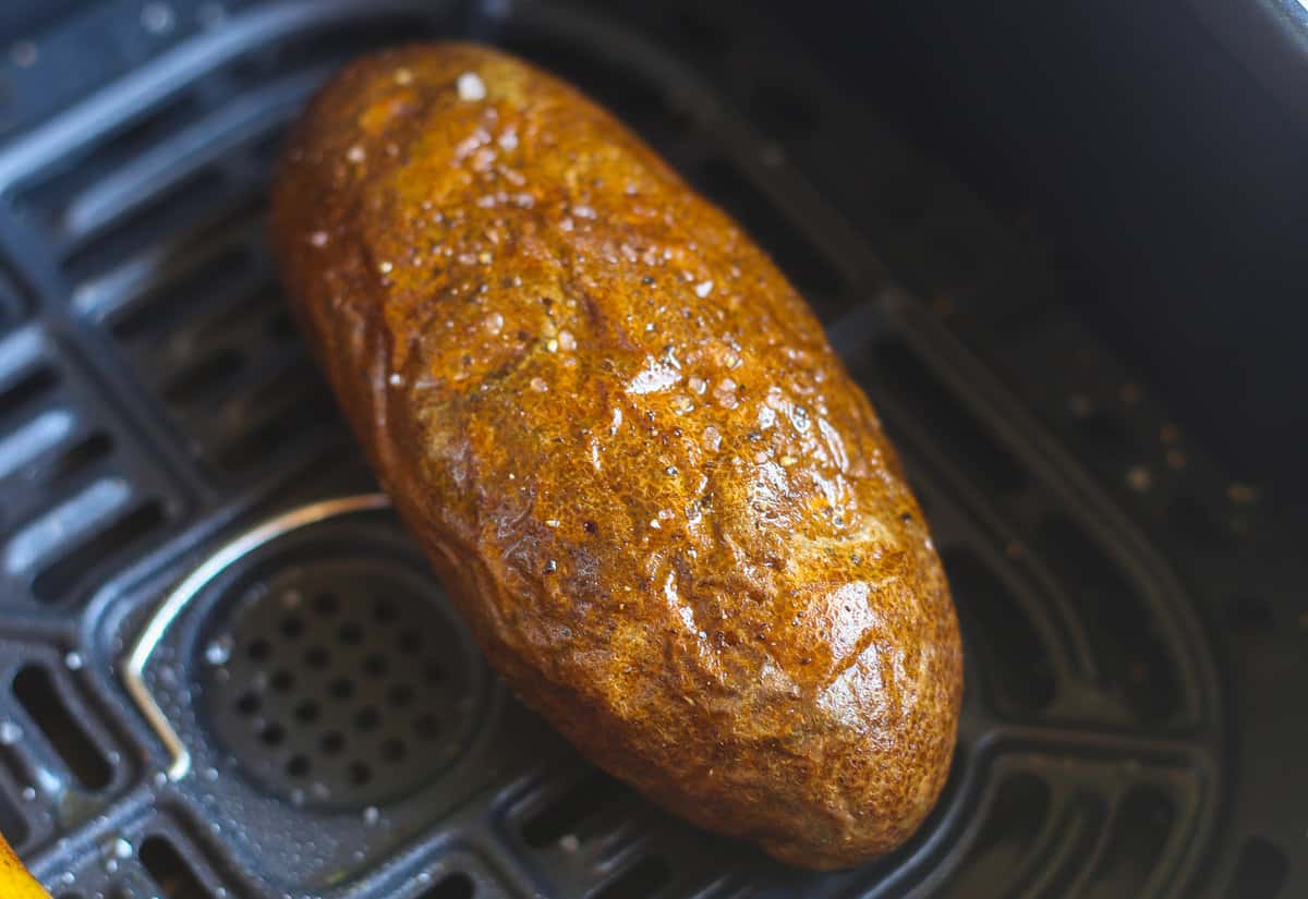 A fully cooked air fryer baked potato still in the air fryer. 