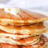 Oatmeal pancakes stacked with butter on top and syrup drizzling down.
