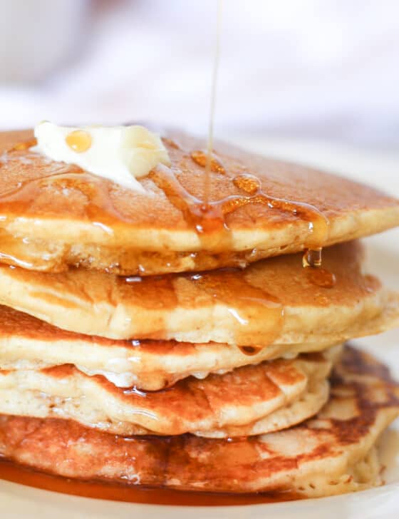 Oatmeal pancakes stacked with butter on top and syrup drizzling down.