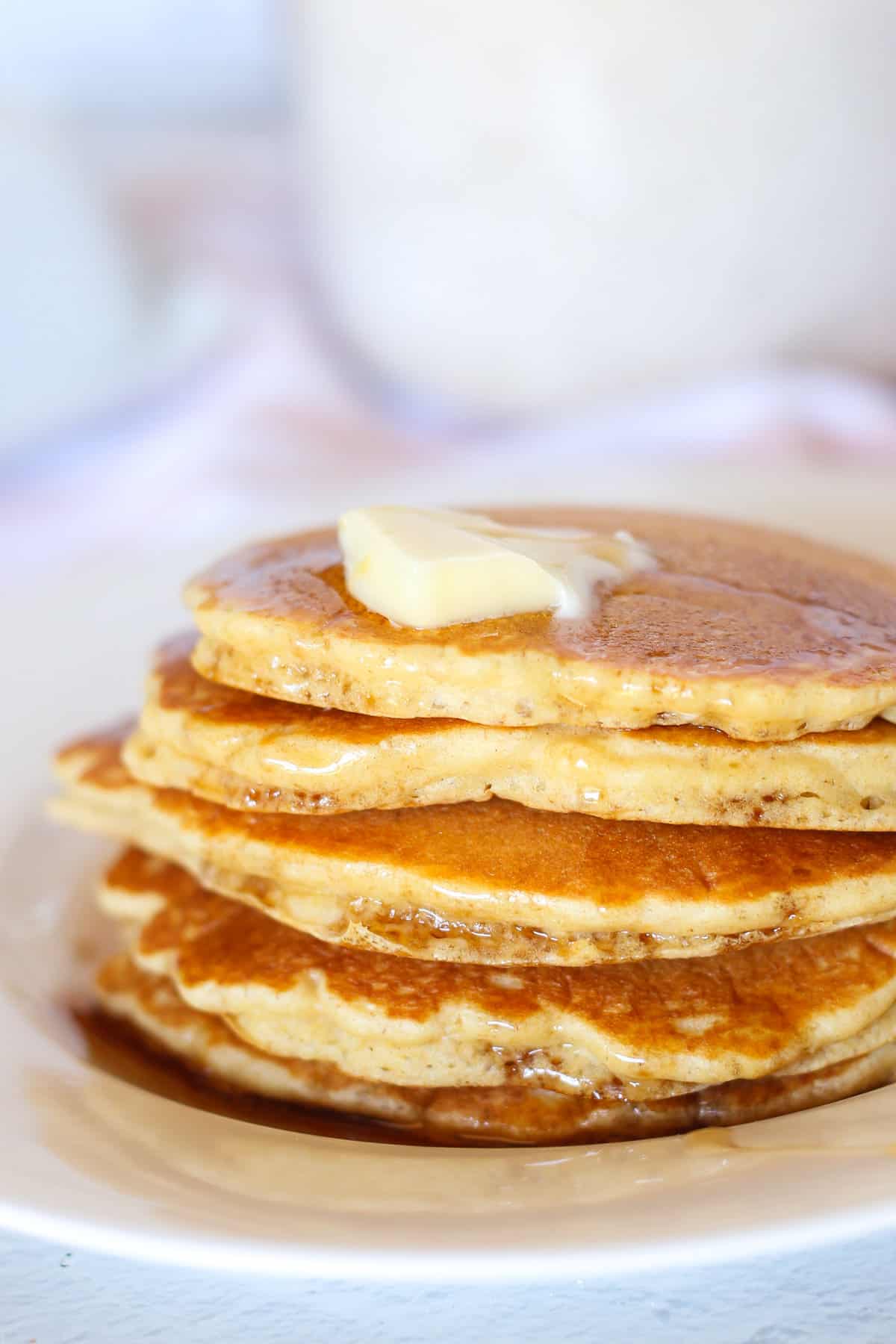 Oatmeal pancakes stacked with butter on top and syrup drizzling down.