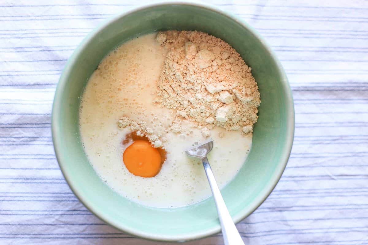 A scoop of oatmeal pancake mix, an egg, and milk being mixed together.