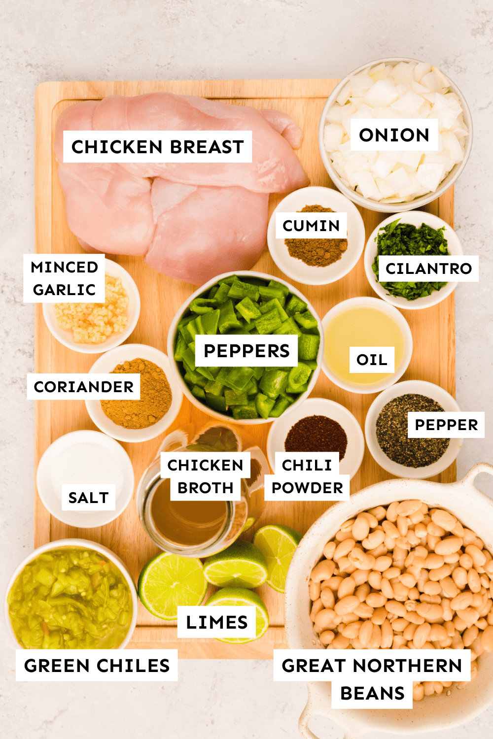 White chicken chili ingredients measured out in bowls on a wooden cutting board and labeled.