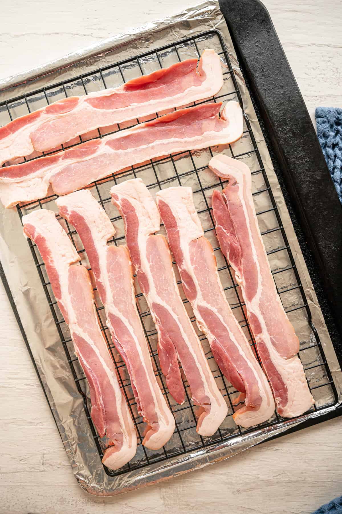 Raw bacon laid out on a cooking rack on top of a baking sheet covered in foil.