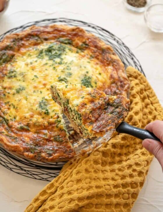 Cooked spinach bacon quiche with a slice being lifted out of the pan with a pie server.