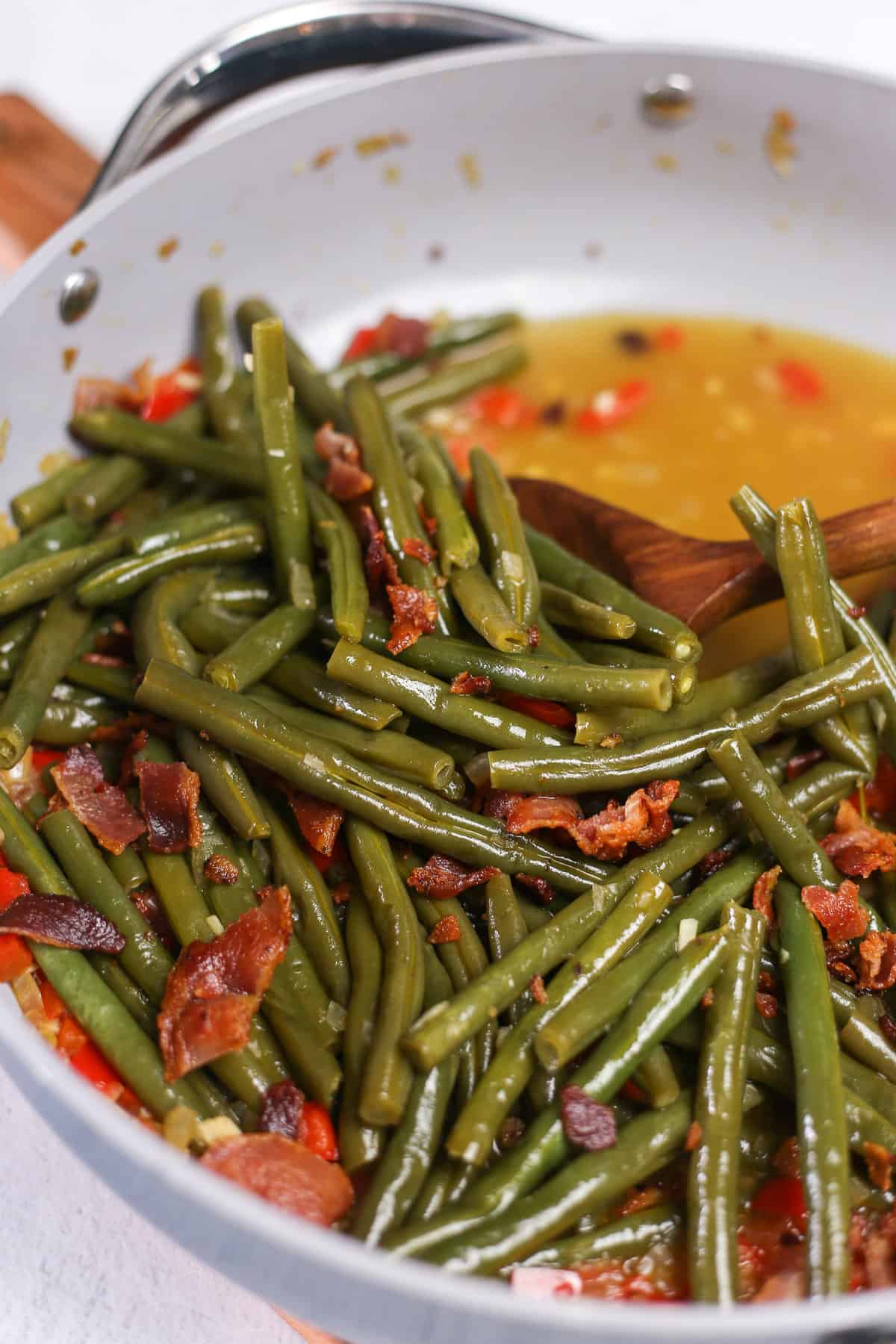 Cooked green beans in a skillet with bacon sprinkled over the top.