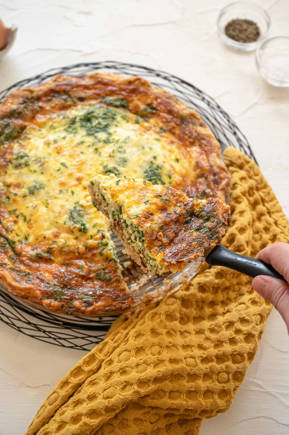 Cooked spinach bacon quiche with a slice being lifted out of the pan with a pie server.