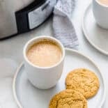 Crock pot filled with pumpkin spice latte recipe and two mugs and cookies too
