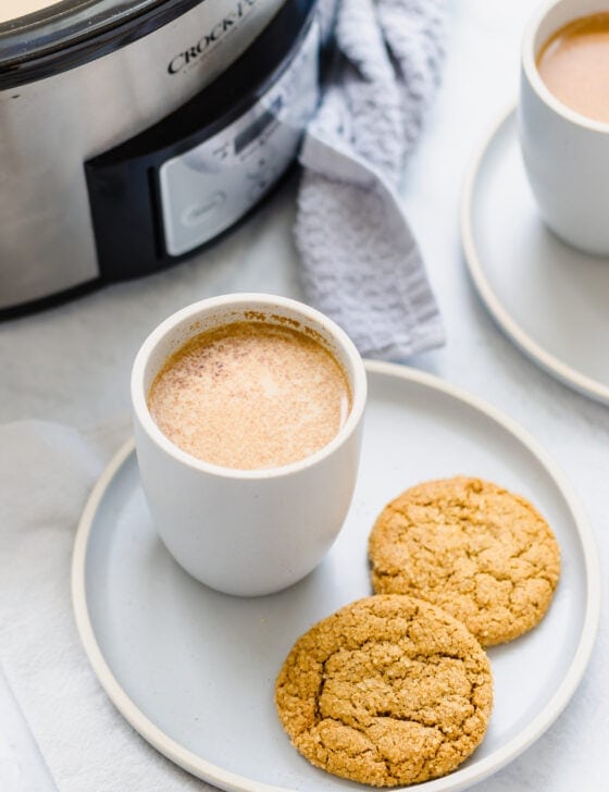 Crock pot filled with pumpkin spice latte recipe and two mugs and cookies too